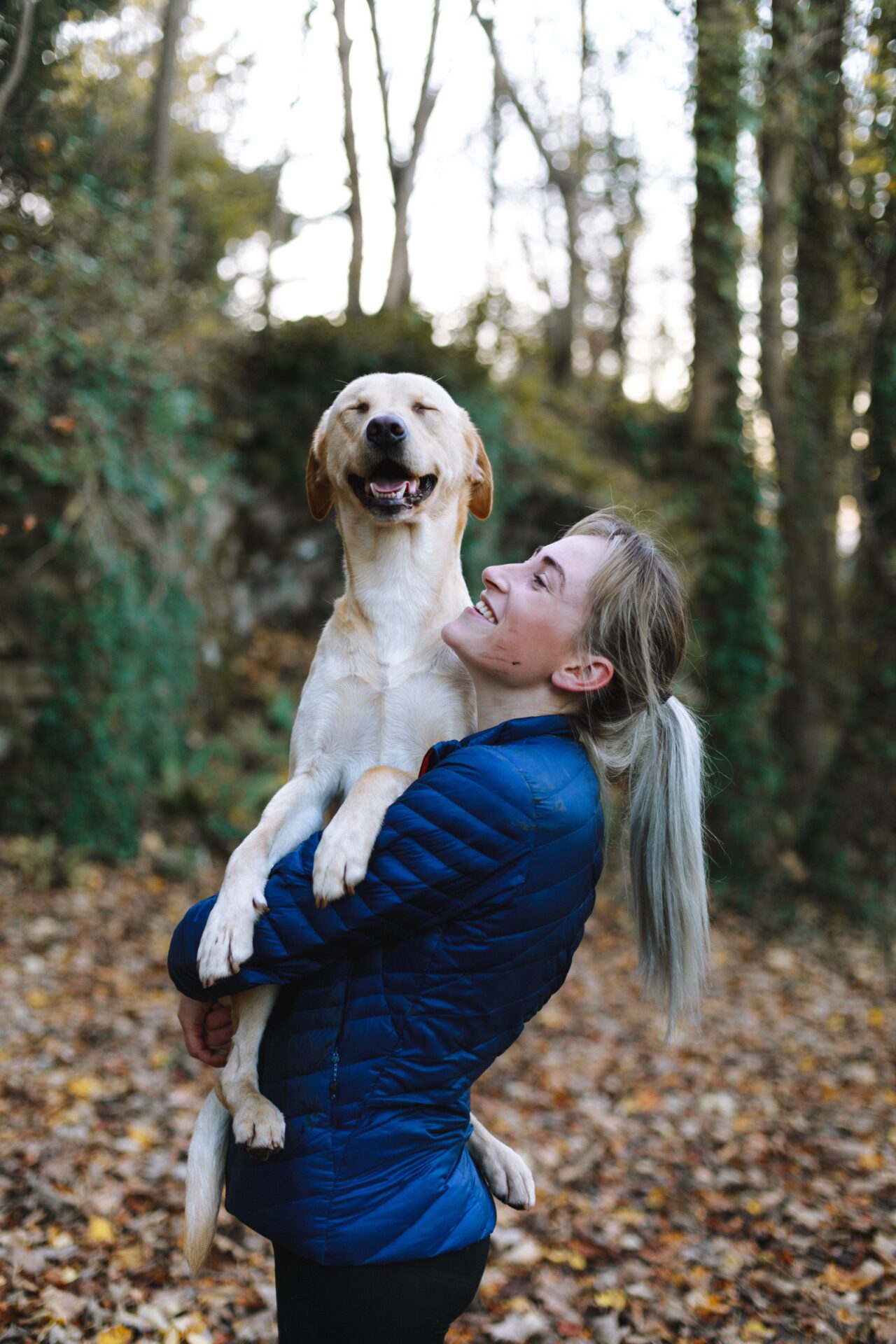 Girl in a forest carrying a happy dog